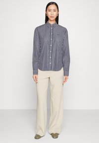 Gestreept overhemd met knopen in marineblauw en wit, voorzien van een kraag, lange mouwen en een getailleerde pasvorm. Gecombineerd met beige broek met wijde pijpen.