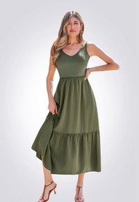 Olijfgroene maxi-jurk met een V-hals, aansluitende bovenkant en gelaagde rok. Gemaakt van geribbeld materiaal, met een split en een losse pasvorm.