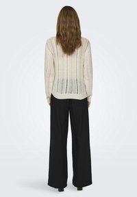 Jasnokremowy sweter z dzianiny w pionowe paski, z długimi rękawami i ściągaczem u dołu. Połączony z szerokimi czarnymi spodniami.
