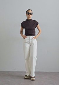 Haut à col montant noir, jean large blanc et chaussures à plateforme à motifs. Les accessoires comprennent des lunettes de soleil noires et des boucles d'oreilles créoles.