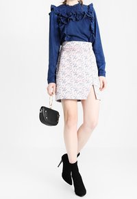 Blouse en denim à volants bleu foncé, associée à une mini-jupe florale rose clair avec une fente sur le côté. Bottines noires et petit sac à main.