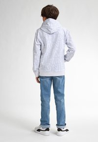 Witte hoodie met groot, omrand tekstpatroon, gecombineerd met lichtblauwe spijkerbroek en witte sneakers met zwarte accenten.