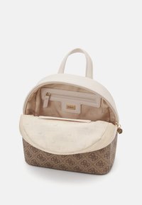 Sac à dos rond en beige et marron, avec un extérieur en cuir lisse et un intérieur en tissu à motifs. Comprend une poche zippée et un accent logo.