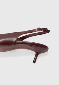 Sandal tumit selutut kulit burgundy dengan desain ramping, ujung runcing, dan tumit stiletto tipis. Dilengkapi dengan gesper perak pada tali.