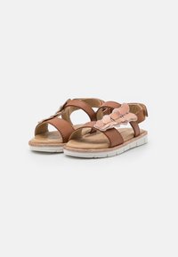 Brown synthetic sandals with cut-out designs, adorned with a pink glittery flower accent. White rubber soles and adjustable straps.