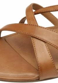 Sandal de cuero marrón con correas entrecruzadas, suela plana, plantilla texturizada y costuras visibles a lo largo de las correas. Diseño simple y minimalista.