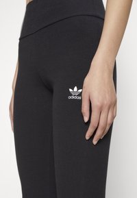 Svarta ribbade leggings med hög midja, prydda med en liten vit Adidas-logotyp på vänstra låret. Materialet ser ut att vara elastiskt.