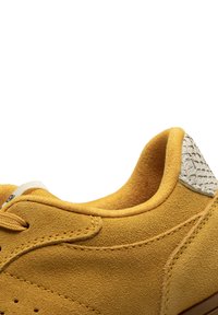 Gelbe Wildledersneaker mit einem strukturierten, cremefarbenen Absatz und kontrastierenden Nähten, ausgestattet mit Schnürverschluss und gepolstertem Kragen.