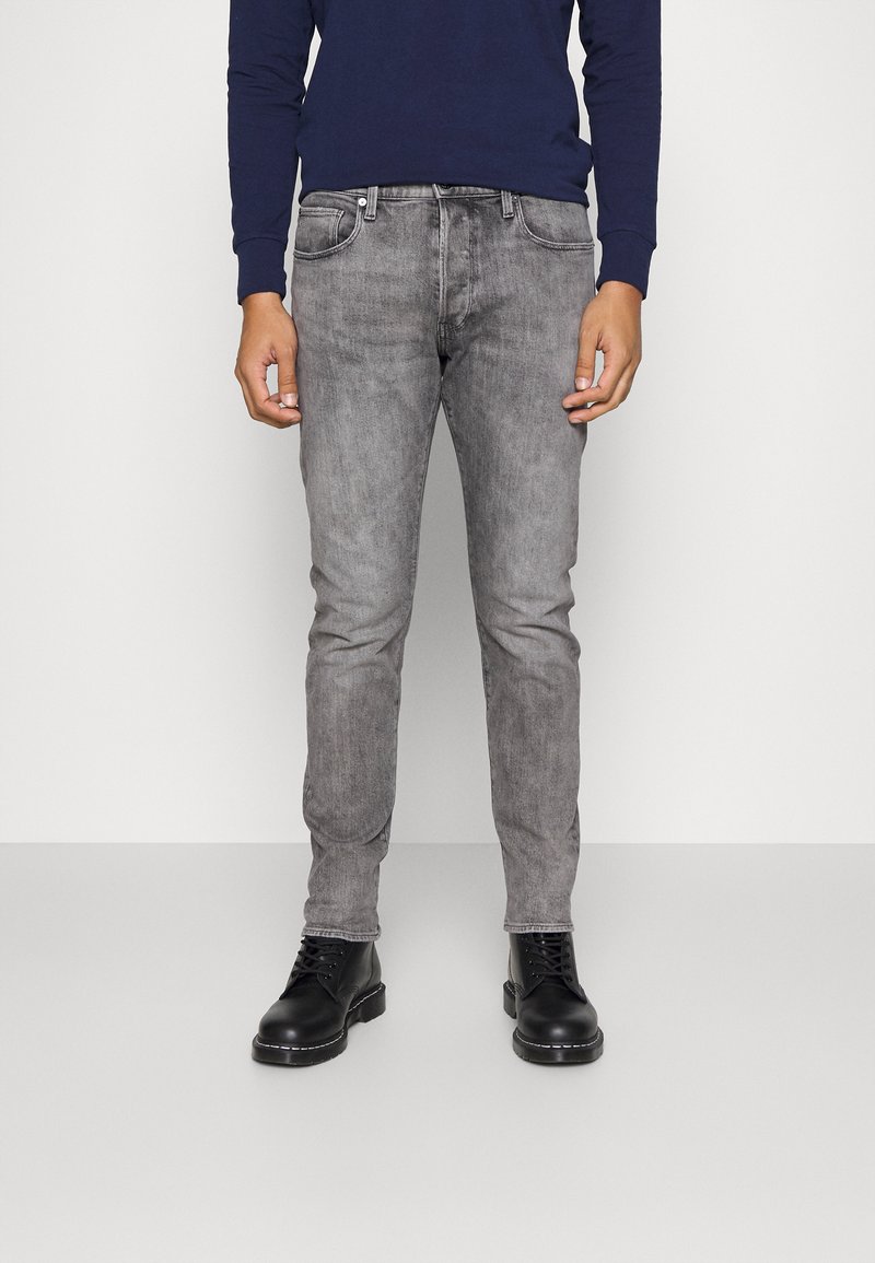 Grå denimjeans med slim fit, fem lommer og subtil falming. Kombinert med svarte snørebåter. Langermet marineblå skjorte synlig.