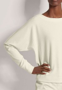 Lichtbeige pullover met ribbelstructuur, brede bootkraag en relaxte mouwen. Opvallend diagonaal quiltpatroon over de stof.