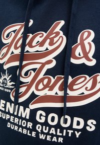 Marineblå hoodie med "Jack & Jones" logo i rød og hvid, med teksten "Denim Goods Superior Quality Durable Wear" og solgrafik siden 1990.