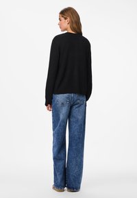 Pull noir à manches longues associé à un jean bleu délavé à jambes larges. Le pull présente un col rond et une coupe décontractée.