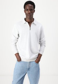 Lichtgrijze sweatshirt met een kwart rits kraag, ribbels aan de mouwen en onderkant. Gekoeld met blauwe denim jeans. Glad materiaal met een casual pasvorm.