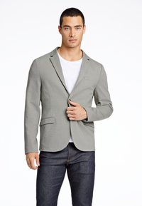 Grå kavaj med slag, två framfickor och en knappstängning. Buren över en vit t-shirt och kombinerad med mörkblå jeans.