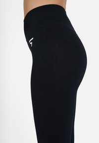Hochtaillierte schwarze Leggings aus dehnbarem Material, mit glatter Textur und seitlichem Logo-Detail. Figurbetonter Schnitt mit nahtlosem Finish.