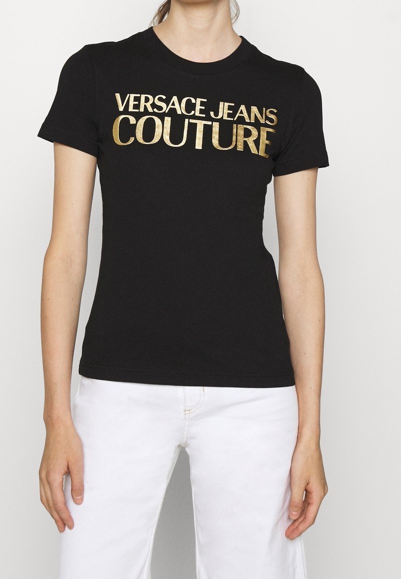 Czarna bawełniana koszulka z dużym złotym napisem "VERSACE JEANS COUTURE". Klasyczny fason z krótkimi rękawami i okrągłym dekoltem.