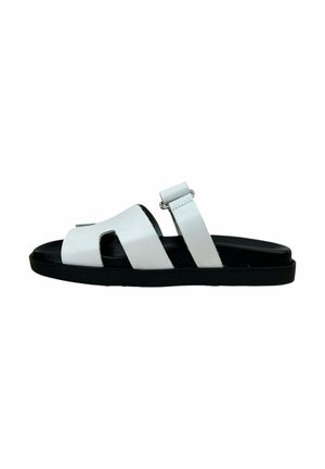 Sandalia deslizante de cuero blanco con dos correas anchas, suela texturizada negra y una correa ajustable en el tobillo. Diseño minimalista con punta abierta.