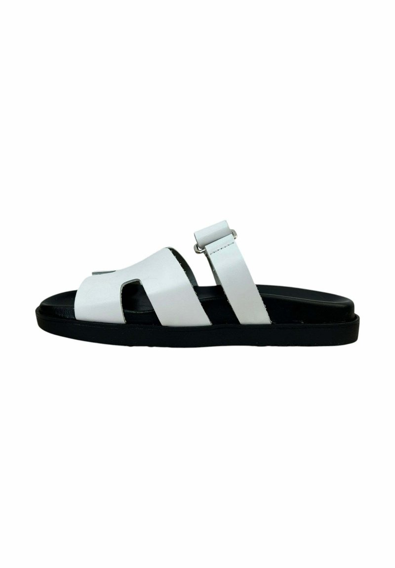 Sandalia deslizante de cuero blanco con dos correas anchas, suela texturizada negra y una correa ajustable en el tobillo. Diseño minimalista con punta abierta.