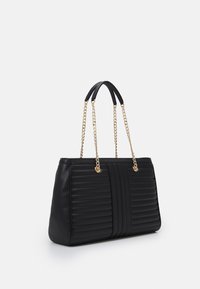 Svart quiltad tote bag med två korta svarta handtag och guldkedjedetalj, placerad mot en vit bakgrund.