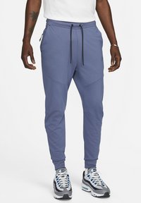 Lichtblauwe sportieve joggers met een zwart trekkoord, twee zijzakken en gestikte details op de benen. Gecombineerd met grijze sneakers.