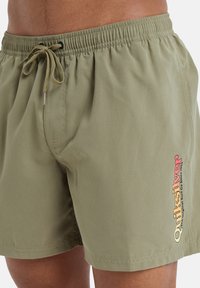 Bañador verde oliva con cinturilla elástica, cierre de cordón y un acento colorido del logo de Quiksilver en el muslo izquierdo.