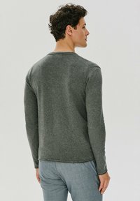 Szara koszula z długim rękawem i okrągłym dekoltem, o miękkiej fakturze i widocznych akcentach szwów. Noszona z jasnoniebieskimi spodniami, które mają swobodny krój.