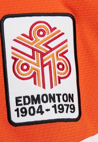 Gestickter Aufnäher mit geometrischem Design in Rot und Orange, Text "EDMONTON 1904-1979" auf weißem Stoff mit schwarzem Rand auf orangefarbener Textilie.