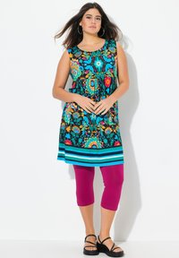 Tunica senza maniche colorata con motivi floreali in turchese, arancione e rosa; abbinata a leggings capri magenta; sandali neri con cinturini.