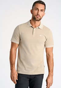 Camiseta polo beige hecha de tejido texturizado, con un cuello, tapeta de tres botones y franjas blancas de acento en las mangas.