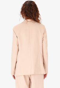 Blazer beige su misura con un design strutturato, maniche lunghe e un retro pulito con dettagli di cucitura sottili.