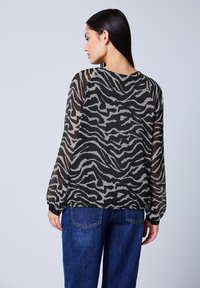 Camicia nera trasparente con stampa zebra grigia, vestibilità comoda, maniche lunghe e scollatura rotonda, abbinata a jeans in denim blu.
