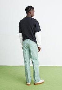 Black cotton t-shirt layered over white long-sleeve tee, paired with mint green trousers and white sneakers with light brown soles.