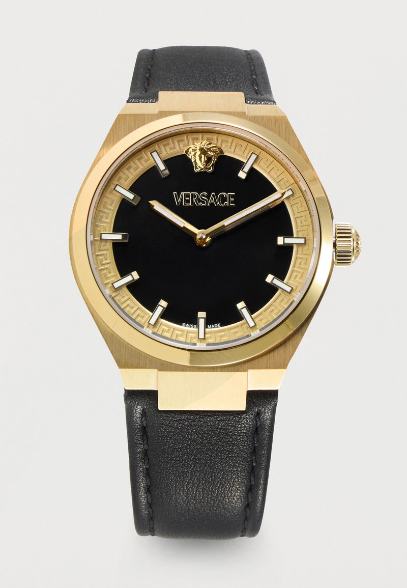 Montre-bracelet Versace dorée et noire avec bracelet en cuir noir, logo Méduse doré et index horaires minimalistes sur cadran noir.