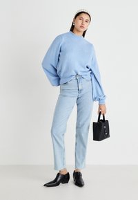 Lyseblå strikkegenser med ballongsleeves, lyseblå høyhårede jeans, svarte spisse ankelstøvletter og en liten svart håndveske.