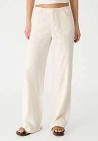 Pantalons larges beige clair avec broderie florale, taille à cordon, texture lisse, présentant une coupe décontractée et des ourlets fendus.