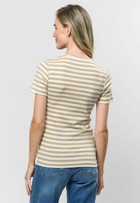 Bežs un balts svītrainais pieguļošais T-krekls ar īsām piedurknēm un noapaļotu kakla izgriezumu, izgatavots no ribotas auduma. Valkāts kopā ar ziliem džinsiem.