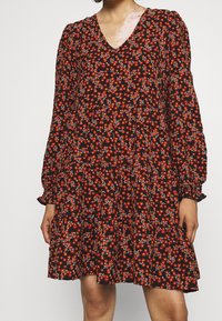 Abito nero con maniche lunghe, scollo a V e motivo floreale in rosso e blu. Presenta una vita arricciata e un orlo svasato. Tessuto morbido.