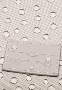 Water-resistant grey textile bag with raised water droplets and a textured surface; features a branded leather patch with debossed text.