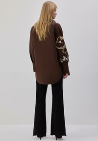 Pruun suurte varrukatega särk, millel on keerukas tikand varrukatel, kombineeritud mustade lehvikpükstega ja kontsakingadega.