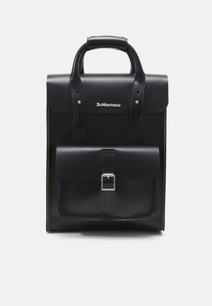 Sac à dos en cuir noir Dr. Martens avec une poche avant à boucle, une poignée supérieure et des coutures jaunes sur les côtés sur fond blanc.