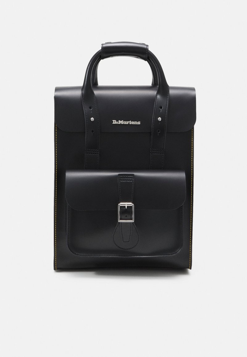 Sac à dos en cuir noir Dr. Martens avec une poche avant à boucle, une poignée supérieure et des coutures jaunes sur les côtés sur fond blanc.