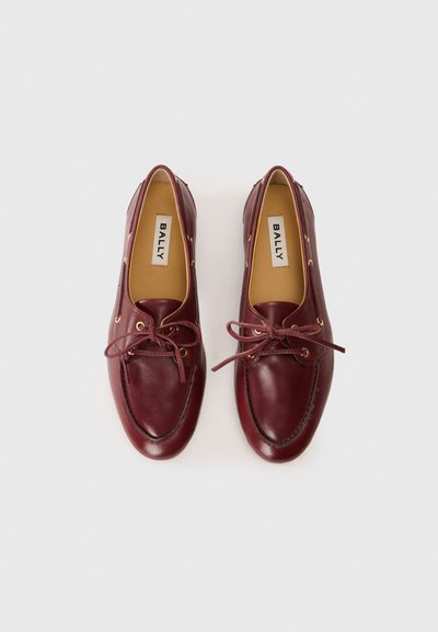 Red leather boat shoes with round toe, lace-up design, gold eyelets, and contrasting stitching. Interior features a light-colored lining.
