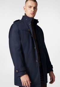 Granatowa wodoodporna kurtka z wysokim kołnierzem, guzikami i bocznymi kieszeniami. Charakteryzuje się gładką teksturą i regulowanymi mankietami.