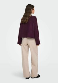 Suéter corto morado con mangas sueltas, combinado con pantalones de pierna ancha beige y botas negras gruesas. Tejido suave, ajuste relajado, minimalismo en los detalles.