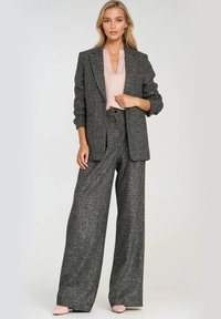 Szary, teksturowany garnitur z dopasowaną marynarką i szerokimi spodniami, w zestawieniu z jasnoróżową bluzką. Gładki materiał i zorganizowany krój.
