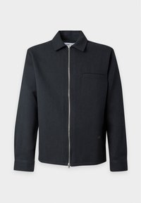 Veste noire à manches longues avec col, fermeture éclair argentée intégrale à l’avant, et une poche poitrine unique, présentée sur un fond gris clair.