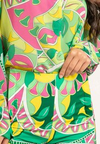 Ensemble de blouse et jupe coloré avec un motif floral vif en vert, rose et jaune. Tissu lisse avec un design ajusté et des détails en boutons.
