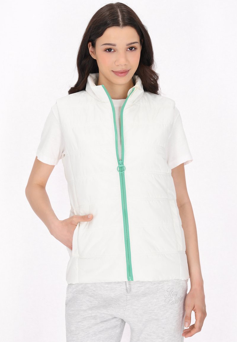 Gilet bianco trapuntato con colletto alto e zip color teal. Abbinato a una camicia bianca a maniche corte e pantaloni felpati grigi.