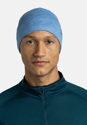 Blue knit beanie with a smooth texture and subtle pattern, worn by a person in a dark teal zip-up top, against a white background.