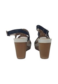 Vista posteriore di sandali strappy blu scuro con tacco a blocco bianco e marrone chiaro. Presenta una fibbia, un design perforato e un segmento del tacco testurizzato.